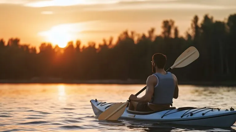 Rear view of man riding kayak in river at sunset.