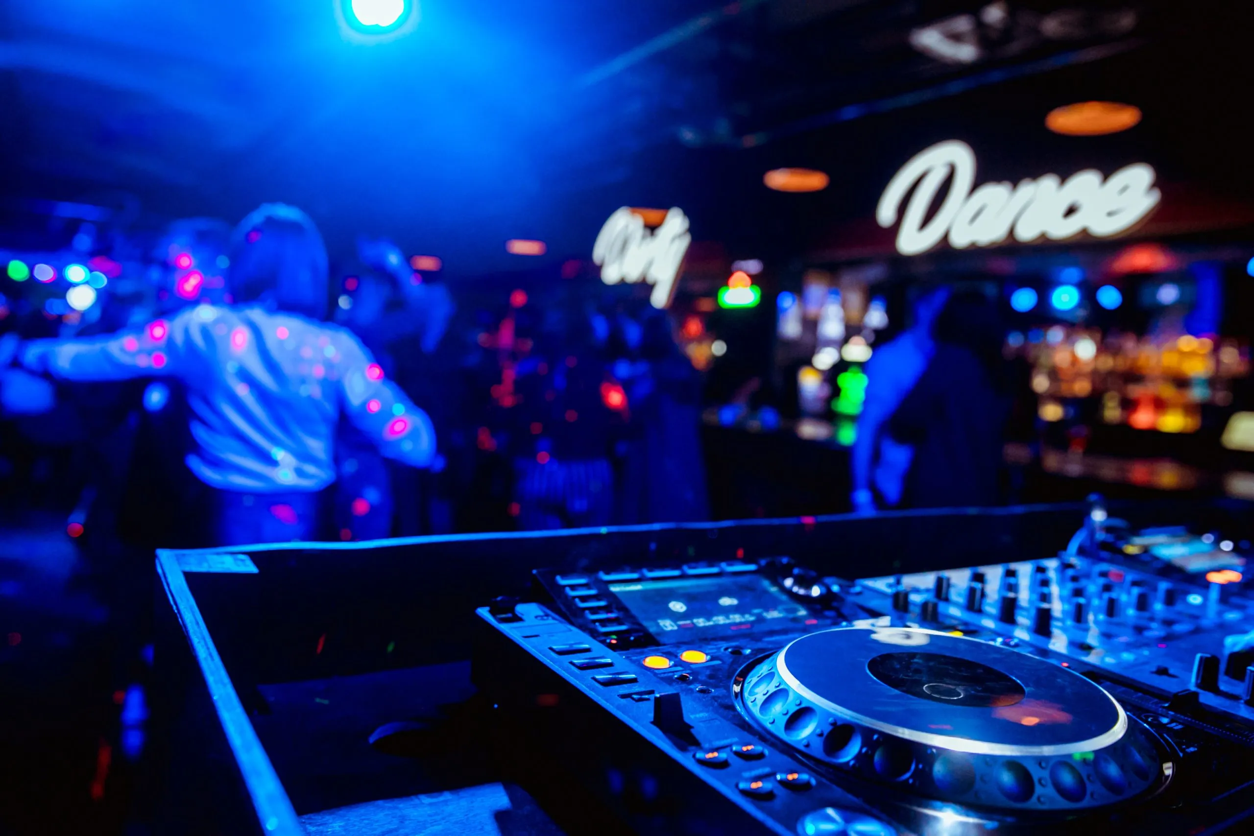 DJ di controllo per il mixaggio di musica con persone sfocate che ballano alla festa in discoteca