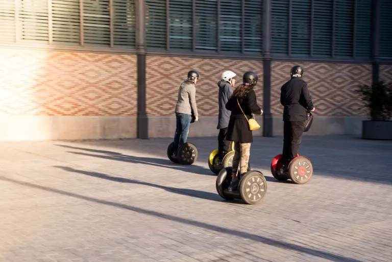 Eine Gruppe von Personen auf umweltfreundlichen Segway-Rollern in einer historischen Straße in Spanien. Touristen, die sich an elektrischen Motorrollern erfreuen.