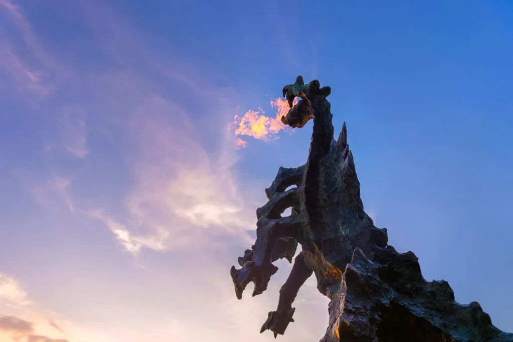 Symbol Krakowa - legendarny pomnik smoka wawelskiego z ogniem wydobywającym się z jego paszczy na tle błękitnego nieba o zachodzie słońca.