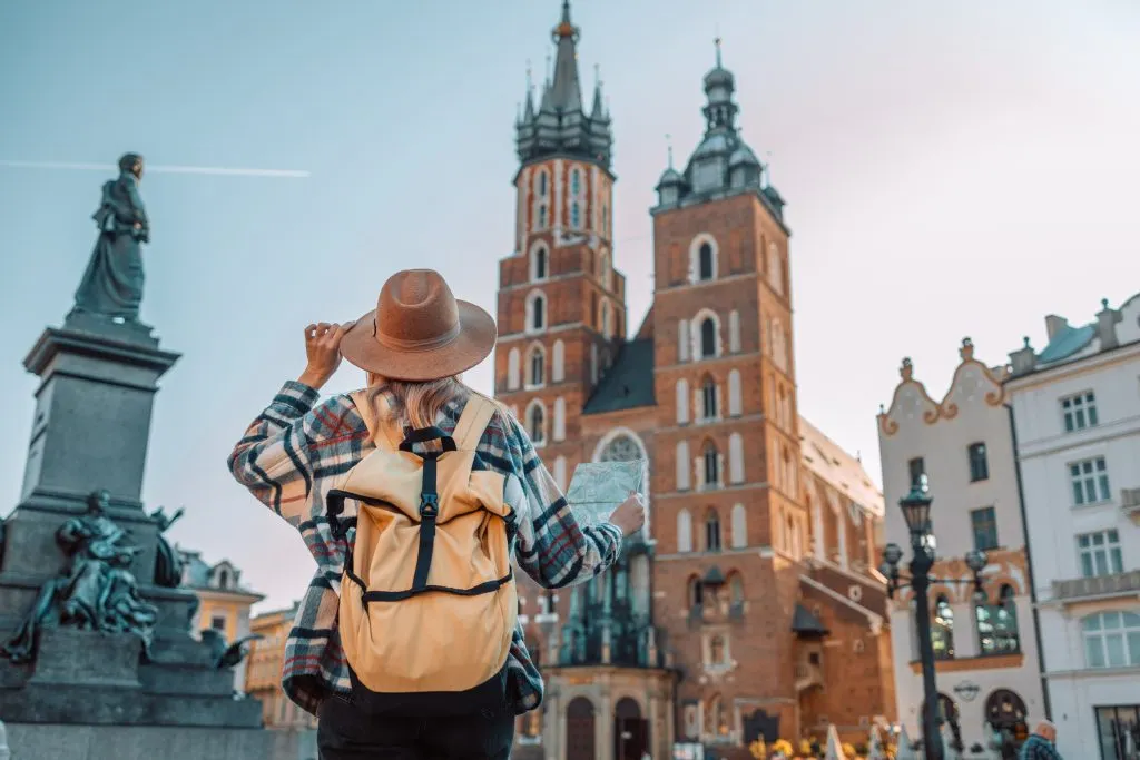 Vista posteriore di una donna viaggiatrice che cammina nella vecchia Piazza del Mercato di Cracovia con in mano una mappa turistica. Concetto di viaggio e stile di vita attivo. Foto di alta qualità